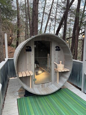 Een houten sauna met een glazen deur, banken binnen en een houten bank buiten.
