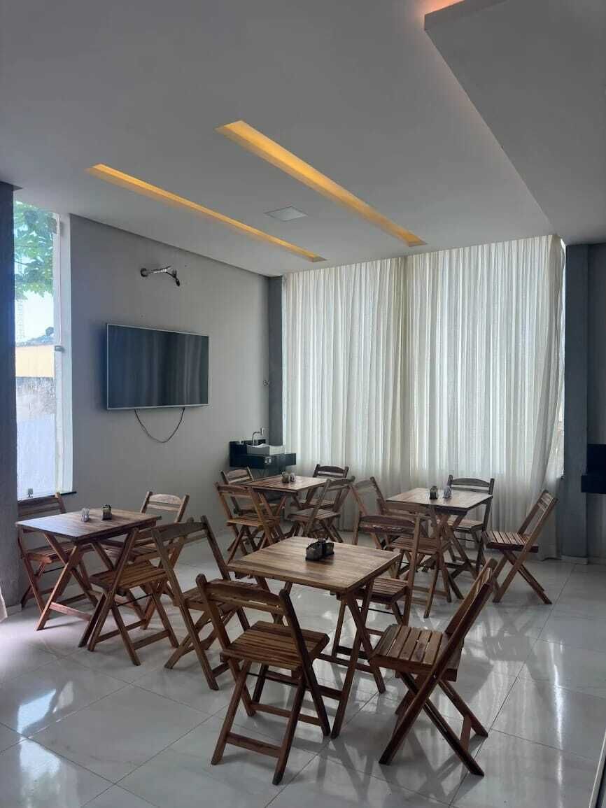 Un comedor moderno con varias mesas y sillas, un televisor de pantalla plana en la pared y un amplio ventanal con cortinas.
