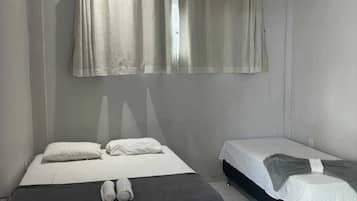 Habitación de hotel con dos camas, ventilador de techo y ventana con cortinas.