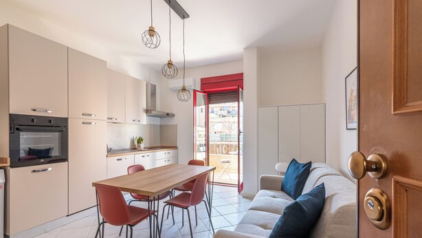 Eine kompakte Küche mit modernen Geräten, ein Essbereich mit roten Stühlen und ein Wohnbereich mit einer Couch und Kissen.