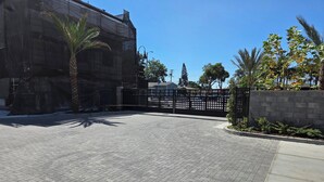 A paved courtyard with a black gate, palm trees, and a building with a mesh facade. - Spacious 4-bedroom townhome in beautiful Long Beach with AC (Long Beach)