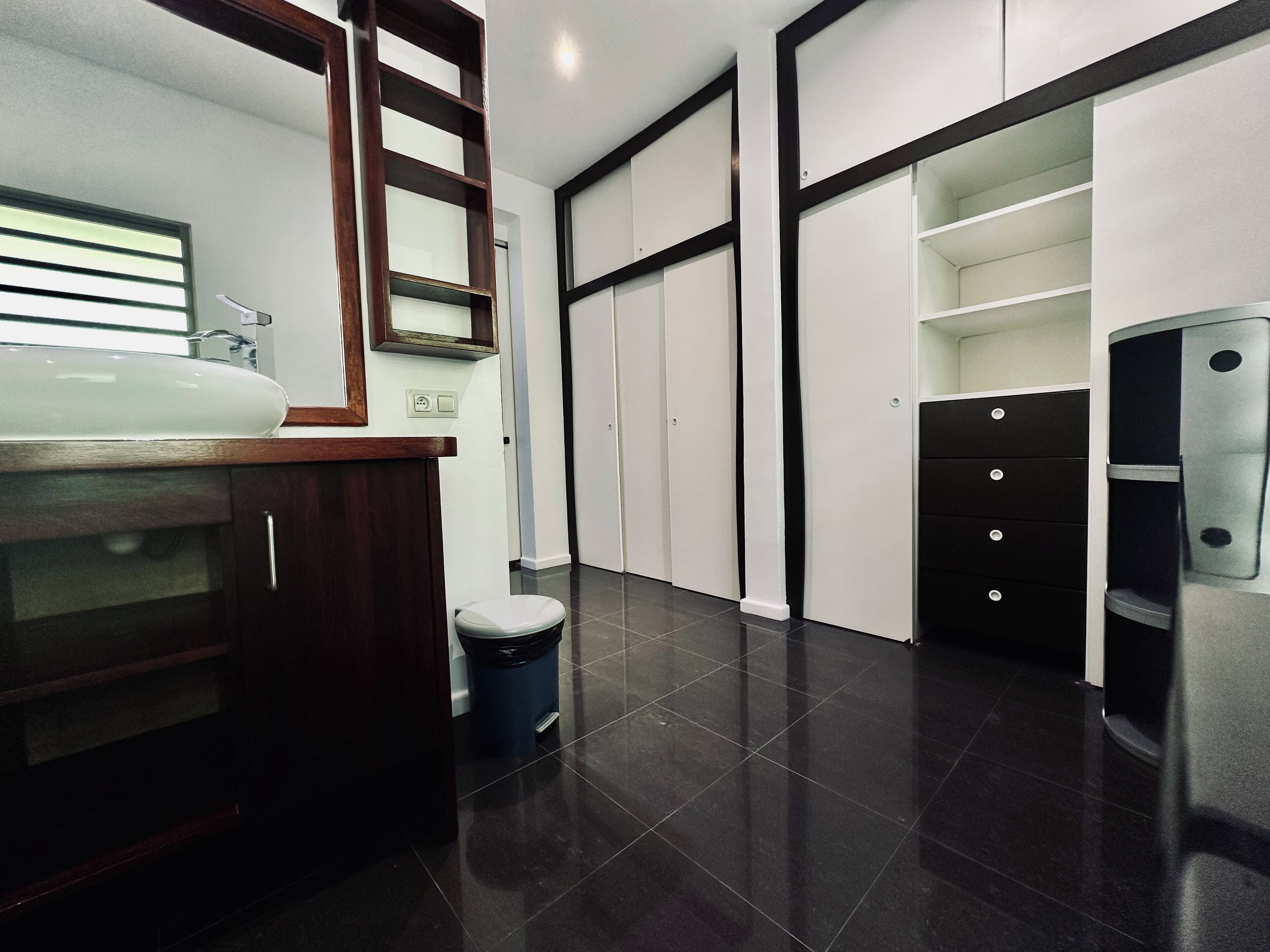 A modern bathroom with a large sink, mirror, and dark tiled floor.