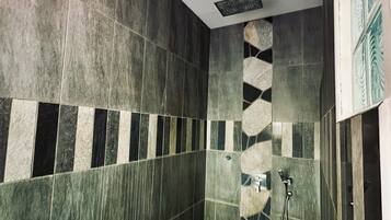 A bathroom with dark green tiles, a stone accent wall, and a shower area with a handheld showerhead.