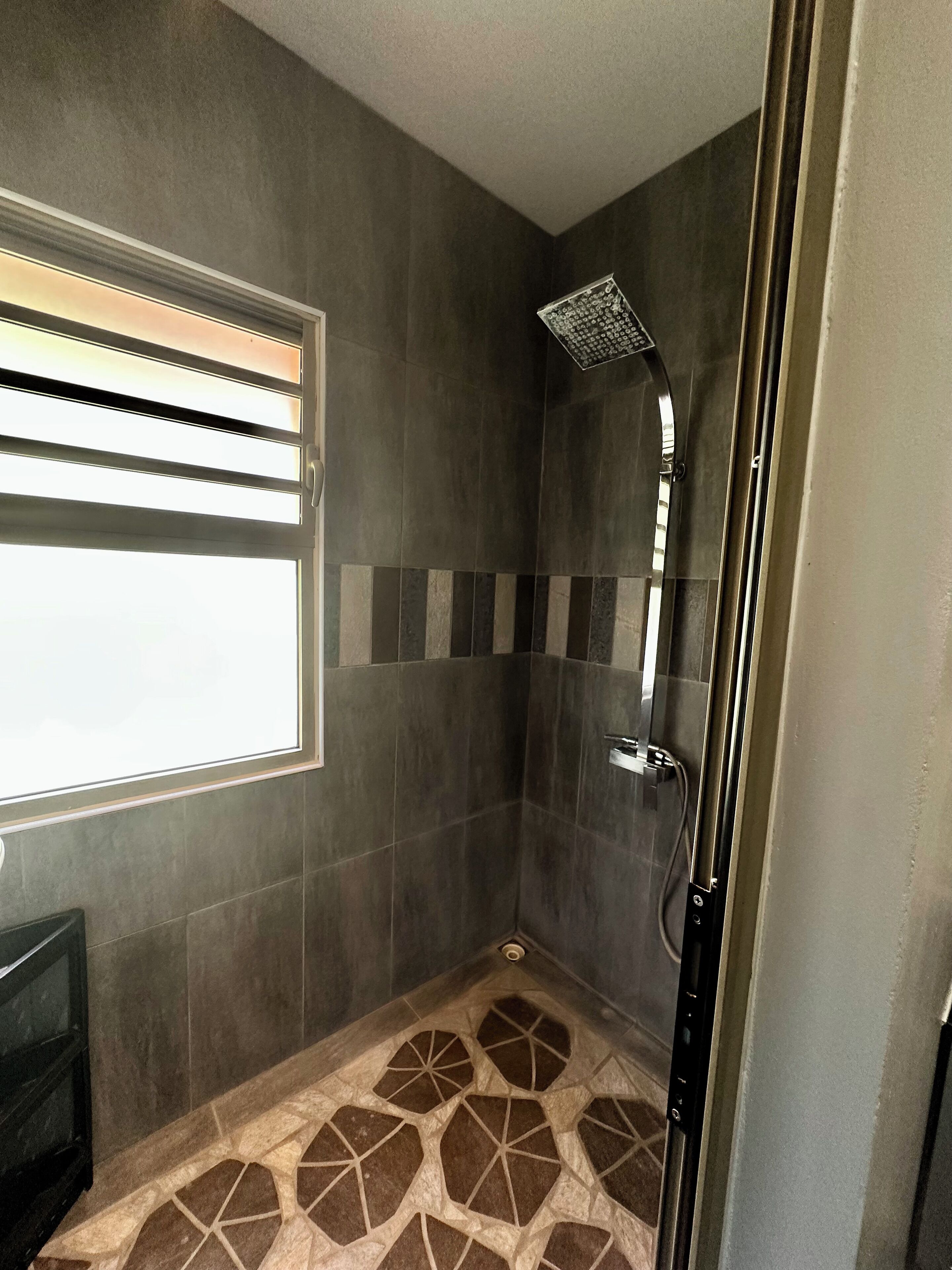 A shower with a rain showerhead, a window with blinds, and a patterned floor.