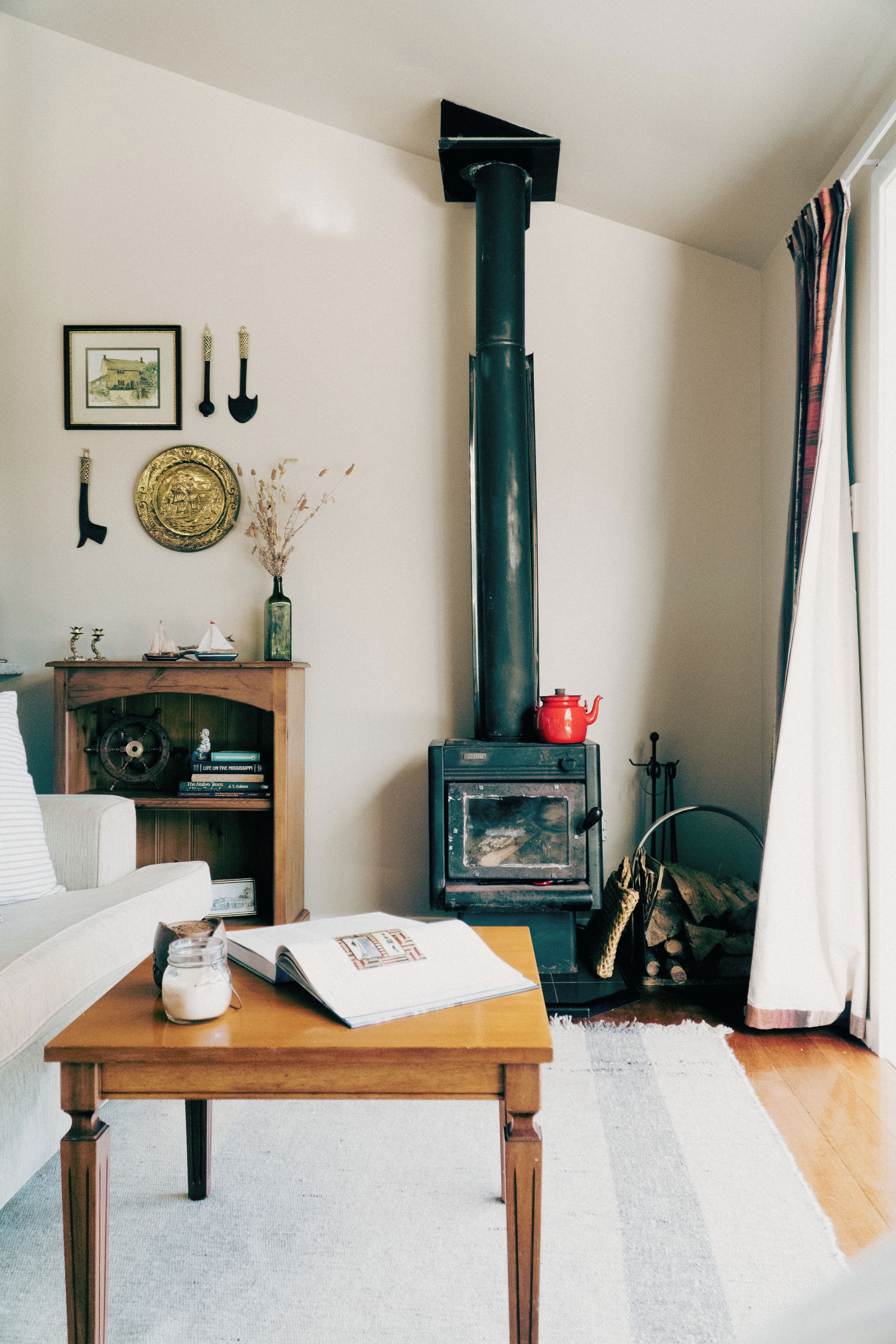 A cozy living room with a wooden coffee table, a sofa, a bookshelf, a decorative wall, and a black stove.
