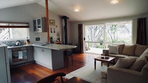 A modern kitchen with an island, a dining area with a sofa and table, and large windows offering a view of trees.