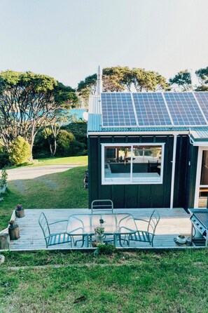 Een klein huis met een dakbedekt met zonnepanelen, een terras met tuinmeubilair en uitzicht op de omliggende begroeiing.