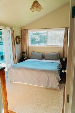 Un dormitorio con cama, ventana, cortinas, mesita de noche y un reloj de pared.