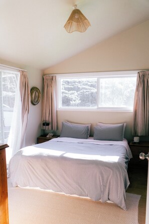 Un dormitorio con una cama grande, dos mesitas de noche, una lámpara de noche, una ventana con cortinas y un colgador de luz.