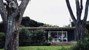 A modern house with a glass facade, surrounded by lush greenery and trees.