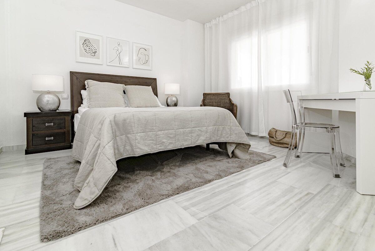 A modern bedroom with a bed, nightstands, a desk, and a chair.