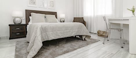A modern bedroom with a bed, nightstands, a desk, and a chair.