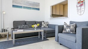 Una sala de estar moderna con un sofá gris, una mesa de centro con flores y una decoración de tabla de surf en la pared.