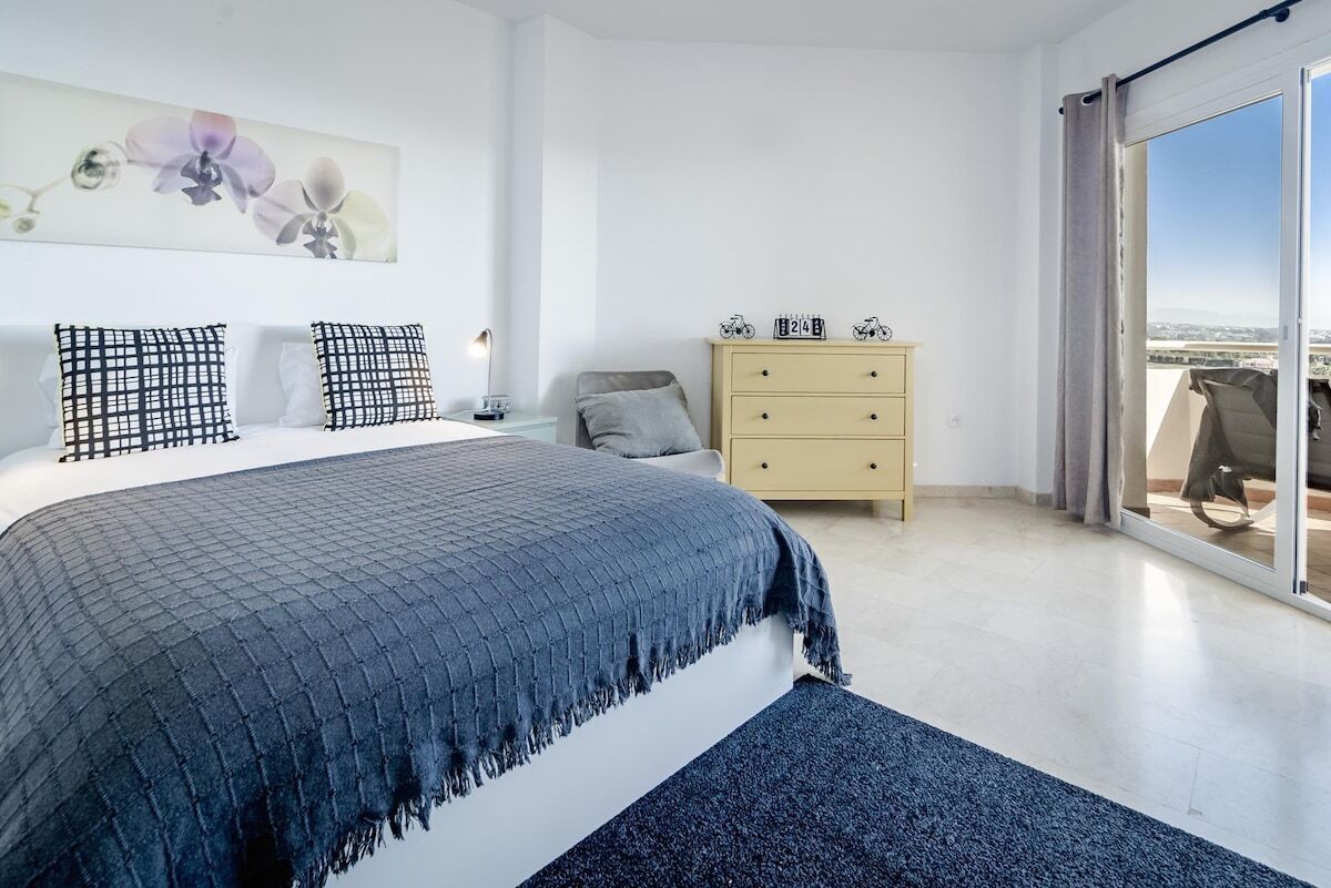 Un dormitorio con cama, cómoda, mesita de noche y un amplio ventanal con vistas.