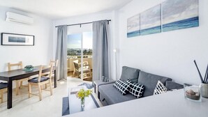 Una sala de estar moderna con un sofá gris, una mesa de comedor con sillas y vistas al mar a través de amplios ventanales.