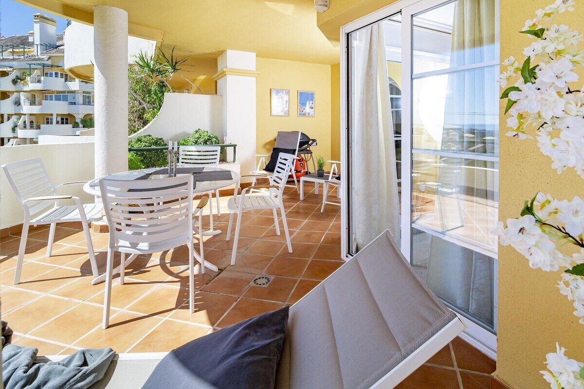 Un balcon avec des chaises blanches, une table et un barbecue.
