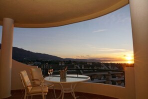 Ein Balkon mit Tisch und Stühlen mit Blick auf eine Stadtlandschaft bei Sonnenuntergang.