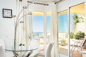 Ein Zimmer mit Glastisch, weißen Stühlen, einer Uhr und Meerblick durch große Fenster.