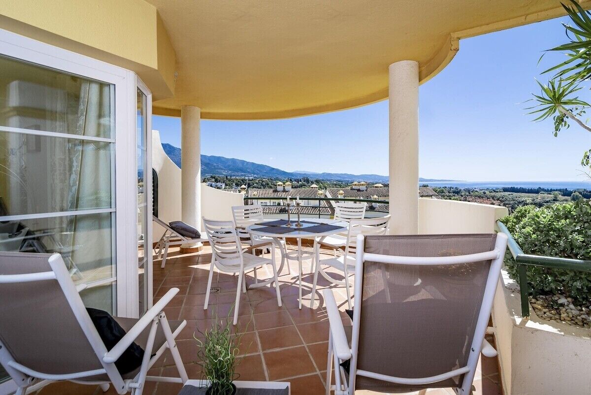 A terrace with a table and chairs, a potted plant, and a view of the landscape.