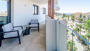 Ein Balkon mit einer Couch und einem Tisch, mit Blick auf eine Straße mit Palmen und Gebäuden.