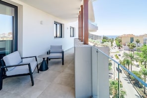 Varanda com sofá e mesa, com vista para uma rua com palmeiras e edifícios.