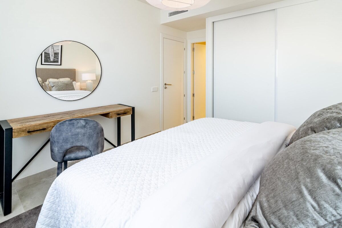 A bedroom with a bed, a desk, a chair, a mirror, and a door.
