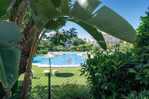 A swimming pool surrounded by greenery, a fence, and buildings in the background. - Dn11-2 Bedroom Apartment Close to Puerto Banus (Marbella)