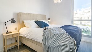 A bedroom with a bed, bedside lamps, a window, and a hanging light fixture. - Lm12b- Exclusive 2 Bedroom Apartment in Le Mirage (Estepona)