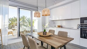 A modern kitchen with white cabinets, a wooden dining table, and two hanging light fixtures. - Lm12b- Exclusive 2 Bedroom Apartment in Le Mirage (Estepona)