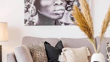 Una sala de estar con sofá, almohadones, una mesa de centro y elementos decorativos como un jarrón y libros.