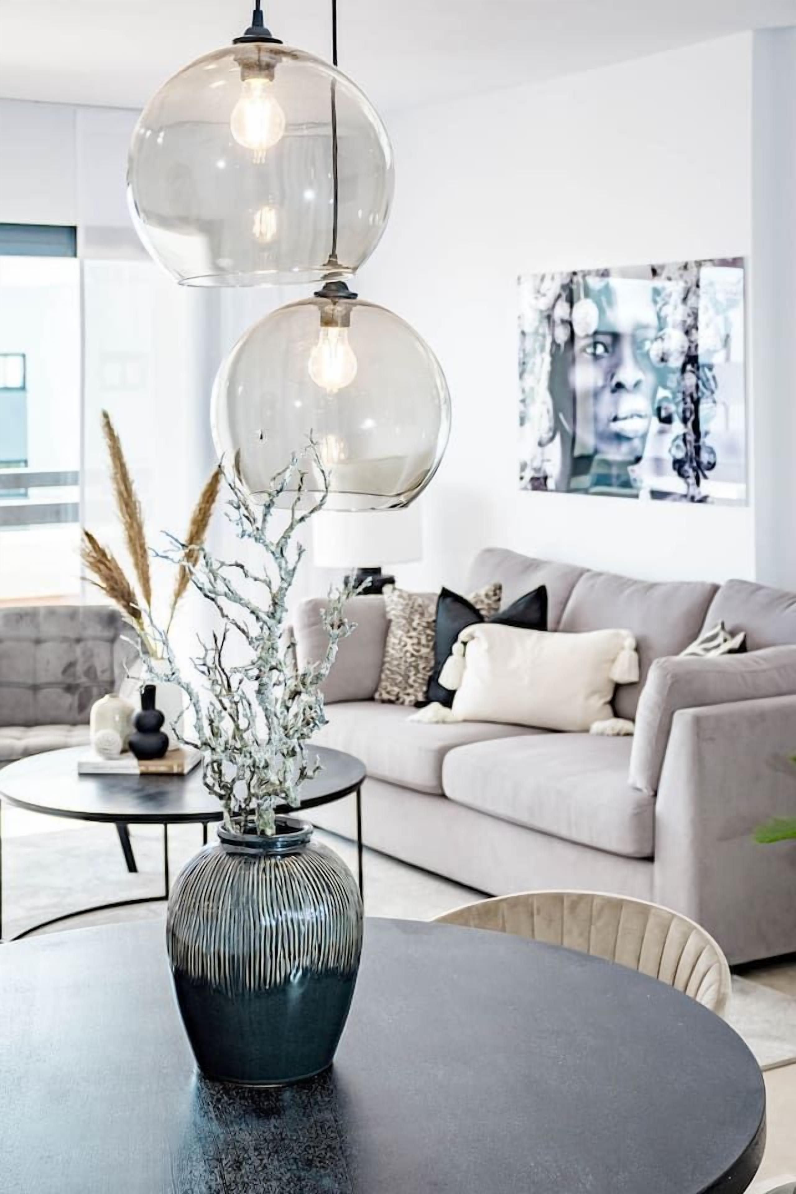 A modern living room with a round coffee table, a vase with branches, a sofa with cushions, and a large abstract painting on the wall.