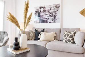 Uma sala de estar com sofá, mesa de centro e objetos decorativos, incluindo um vaso com plumas de capim-do-campo e um livro.