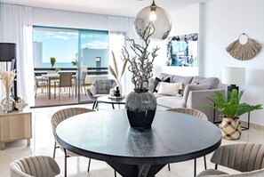 A modern living room with a round table, sofa, and chairs, a dining area, and a view to the outside. - Dja- Modern 2 Bedroom Apartment Close to Beach (Casares)