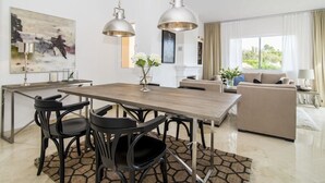 Un salon moderne doté d’une grande fenêtre, d’un coin repas avec une table en bois et des chaises noires, et d’un canapé beige.