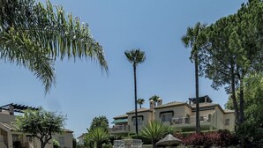 Une piscine à l’eau d’un bleu limpide, entourée d’une terrasse carrelée, et un bâtiment avec un balcon en arrière-plan.