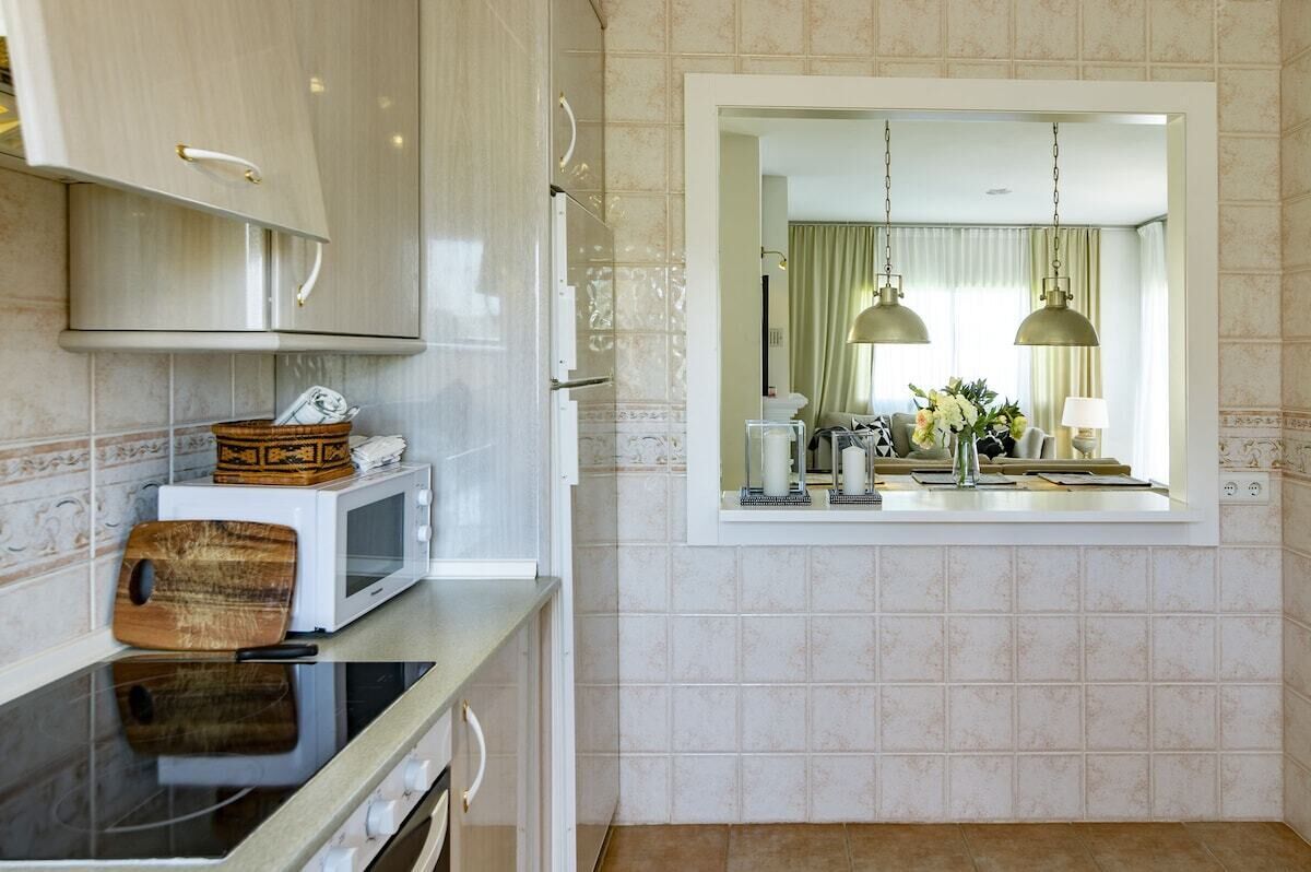 A modern kitchen with white cabinets, a microwave, and a wooden cutting board.