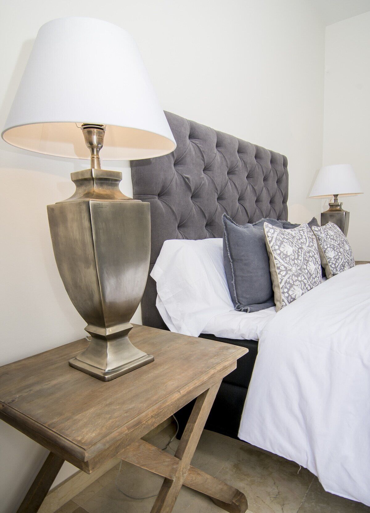 A neatly made bed with white and gray linens, a tufted headboard, and a bedside table with a lamp.