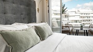 Une chambre d’hôtel avec un grand lit, une vue sur la ville par la fenêtre et un balcon équipé de chaises et d’une table.