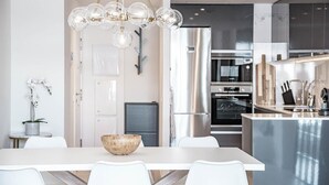 Une cuisine moderne dotée d’appareils électroménagers en acier inoxydable, un coin repas blanc agrémenté d’un centre de table en forme de saladier en bois, et un lustre original.