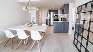 Une cuisine moderne dotée d’un îlot central, d’appareils électroménagers en acier inoxydable et d’un coin repas avec une table et des chaises blanches.