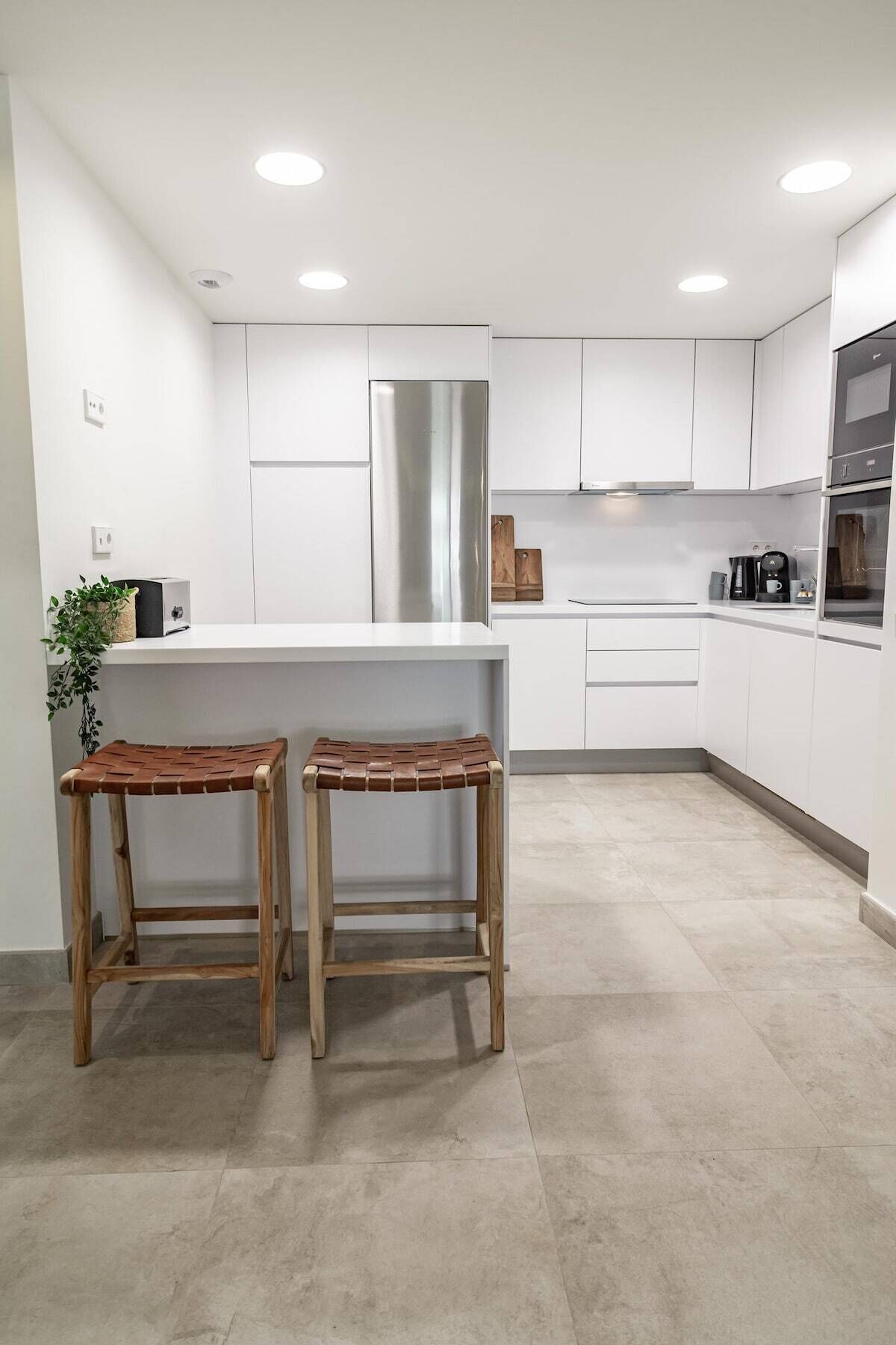 A modern kitchen with white cabinets, a stainless steel refrigerator, and two wooden stools.