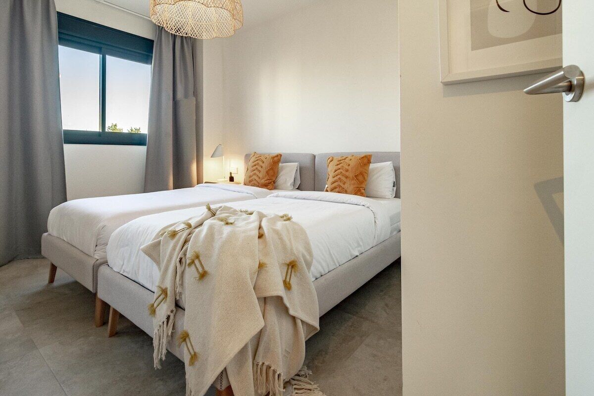 Quarto com cama de casal, duas almofadas, abajur e janela com cortinas.