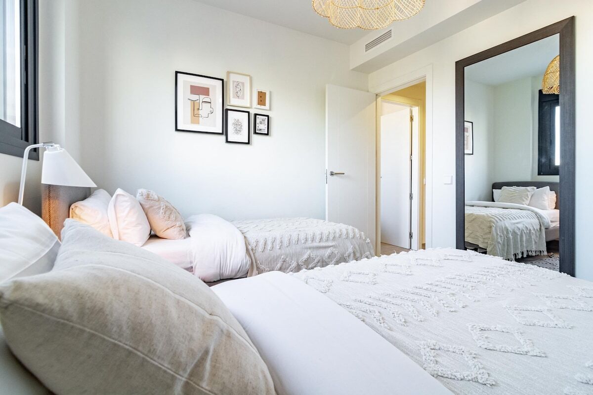 A bedroom with two beds, a bedside table, a lamp, and framed artwork on the wall.