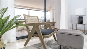 Een moderne woonkamer met een houten stoel, een grijze poef en een vloerlamp.