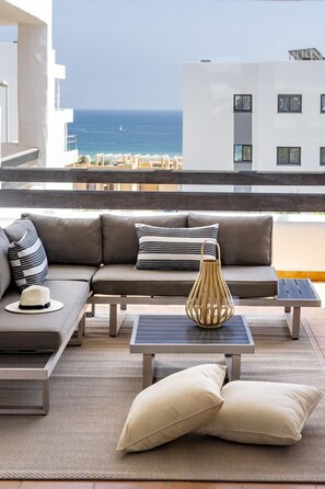 A balcony with a sofa, a table, and a view of the sea. - Djc- Modern 2 Bedroom Apartment Close to Beach (Casares)