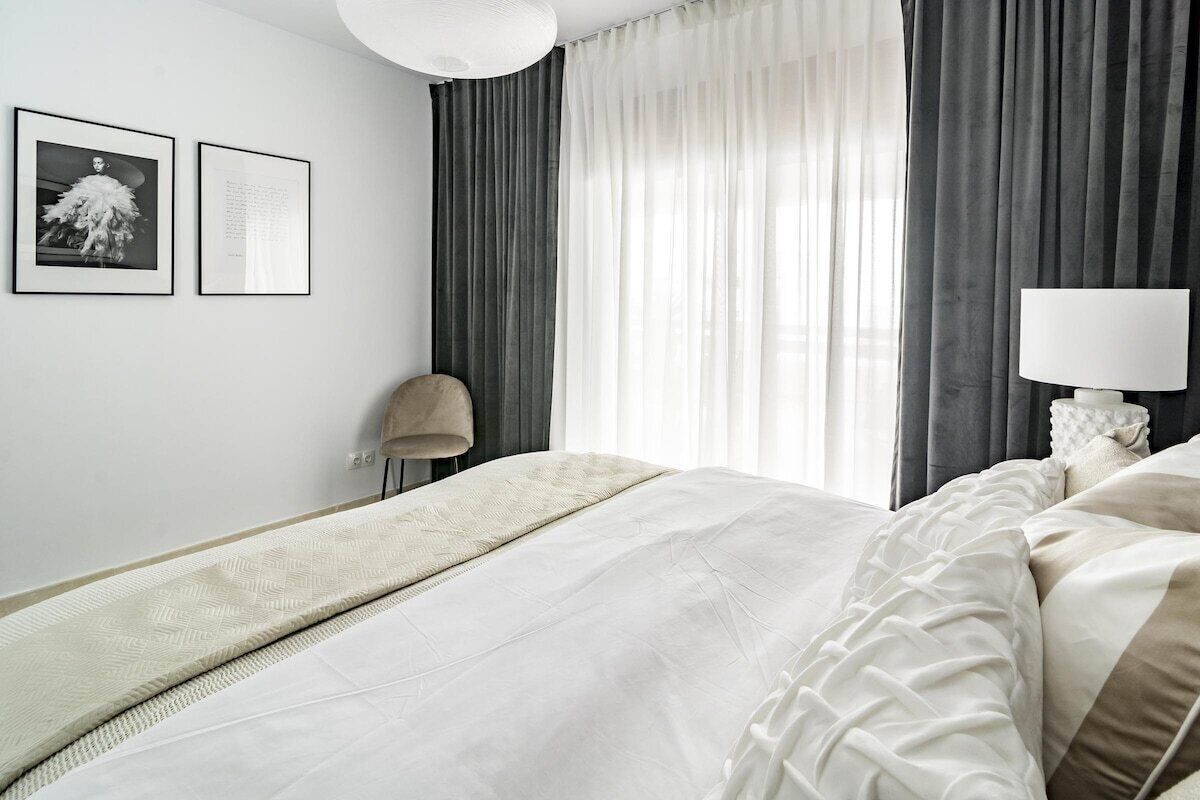 Habitación de hotel moderna con una cama grande, una lámpara de noche y una silla. Hay dos cuadros en la pared.