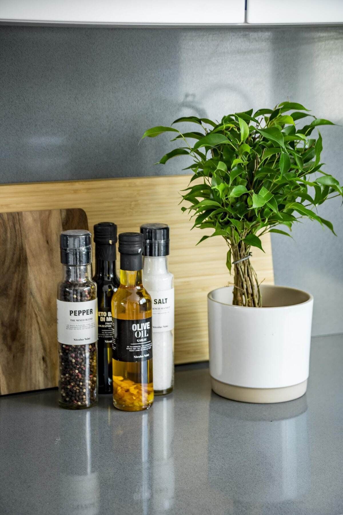 Een aanrecht met een potplant, een houten snijplank en flessen peper, olijfolie en zout.