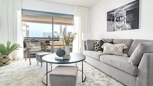 Een moderne woonkamer met een grijze bank, een ronde salontafel en uitzicht naar buiten.