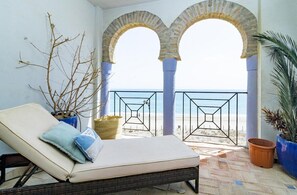 A balcony with a lounge chair, potted plants, and a view of the beach. - Lap- 3 bed Apartment on the Beach. Families Only (Casares)