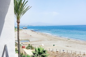A beach view with a palm tree, clear sky, and distant mountains. - Lap- 3 bed Apartment on the Beach. Families Only (Casares)